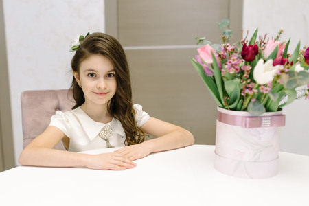 A cute girl sits on a sofa and holds flowers in her hands. Feast dayの写真素材
