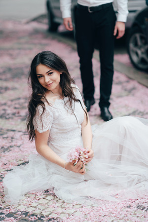 Portrait of a young beautiful brunette girl in white wedding dress sitting in a blooming spring garden.の写真素材