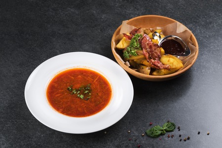 Complex dinner. Fried potatoes with appetizing bacon and sauce are in a wooden plateの写真素材