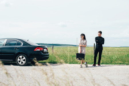 Couple of young girl and boy holding talks near black car on background of blue sky and field.の写真素材
