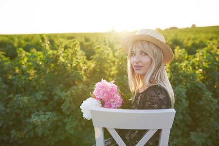 Cute young blond girl sits on a chair against green background with pions in her hands.の写真素材