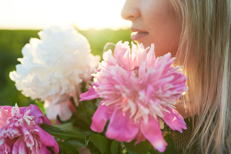 Cute young blonde girl spends time in a picturesque field with a bunch of pions in her hands.の写真素材