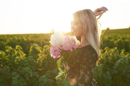 Cute young blonde girl spends time in a picturesque field with a bunch of pions in her hands.の写真素材