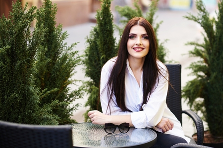 Cute young brunette girl with beautiful professional make-up sitting in a street cafe on a beautiful sunny dayの写真素材