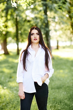 Cute young brunette girl with beautiful professional make-up on green background in parkの写真素材