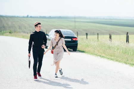 Couple of young girl and boy holding talks near black car on background of blue sky and field.の写真素材