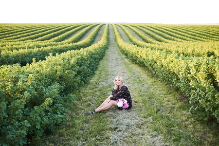 Cute young blonde girl spends time in a picturesque field with a bunch of pions in her hands.の写真素材