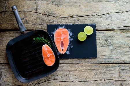 Two salmon steaks are ready to cook on a grill, along with lime on a wooden background. Top view. Healthy food.の写真素材