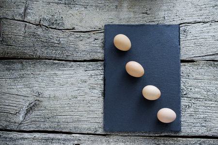 Four raw chicken eggs lie on a black board on a wooden background.の写真素材