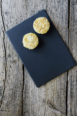 Two muffins, covered with shtryzelem, and with cheese cream on a black board on a wooden background.の写真素材