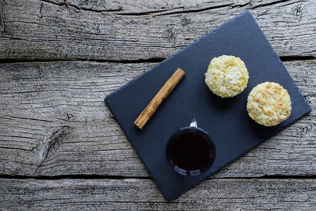 Two muffins covered with shtryzelem and cheesecream on a black board, next to a cup of coffee and a cinnamon stick on a wooden background.の写真素材
