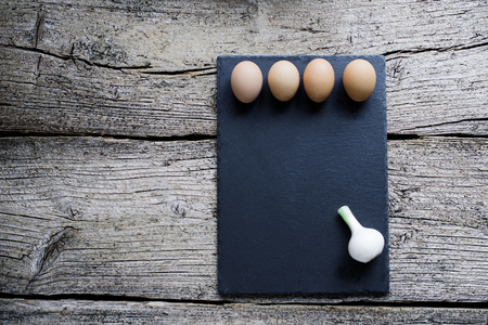 Two raw chicken eggs lie on a black board along with a young onion on a wooden background.の写真素材