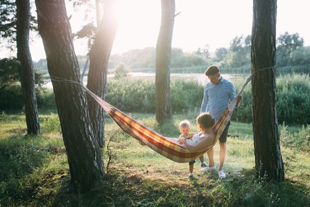 Young sympathetic family - mom, dad and son rest in the nature, sitting in a hammockの写真素材