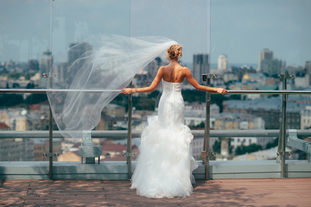 Bride in the morning in a white dress standing on the balcony overlookin the city.の写真素材