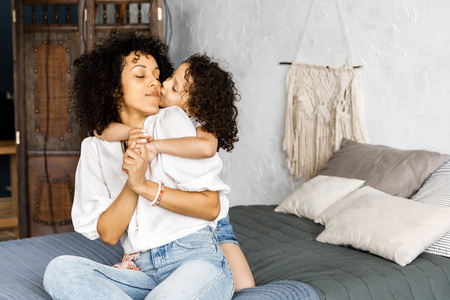 Mom and little cute curly girl spend time together, hugging and kissing each other.の写真素材