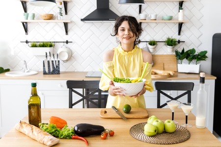 Young pretty woman cuts an avocado on a wooden salad board. Cooking.の写真素材