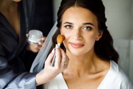 Young woman stylist doing makeup beautiful bride in beauty salonの写真素材