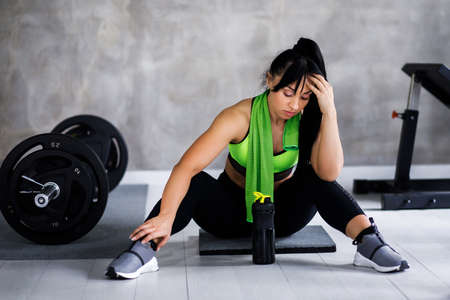 Beautiful young woman looking away while sitting on exercise mat at gymの写真素材