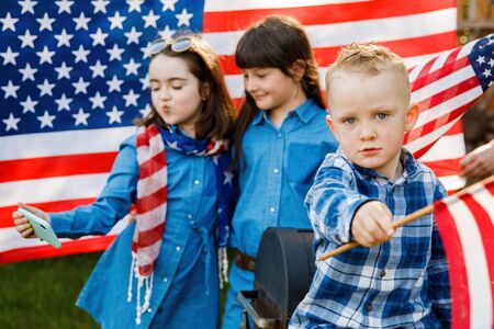 Cute blond boy and two girls have fun on the street on the background of the American flag. Independence Day