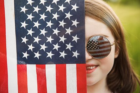 Pretty young pre-teen girl in field holding American flag. Independence Day