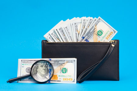 Black wallet with one hundred dollar bills on a blue backgroundの写真素材