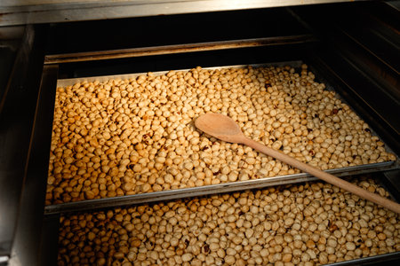 Freshly roasted nuts glisten under warm lighting in a bustling kitchen as a wooden spoon rests atop a tray of golden delicaciesの写真素材