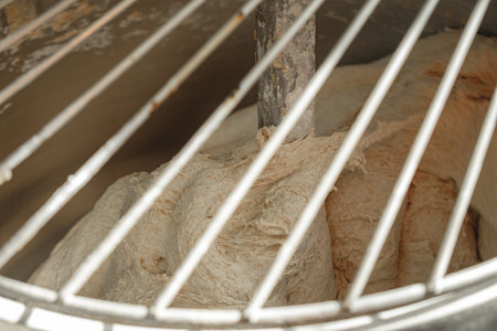 Dough kneading process in a bakery kitchen, showcasing the blending of ingredients into a smooth,...