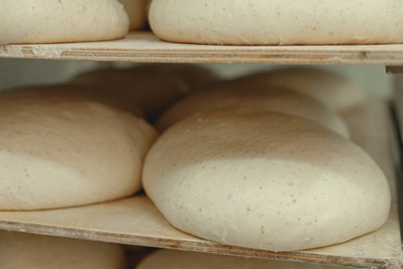 Freshly prepared dough resting on wooden racks in a cozy bakery during the early morning hours,...