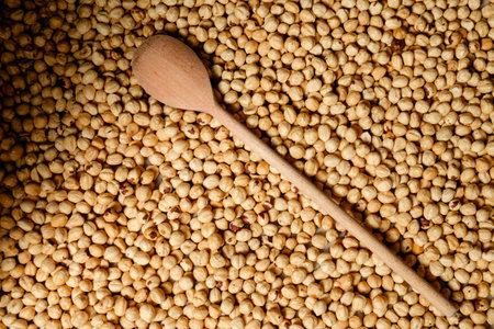 Natural wooden spoon resting on a bed of toasted chickpeas in a rustic kitchen with warm lightingの写真素材