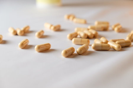 Golden capsules scattered across a white surface in soft natural lightの写真素材