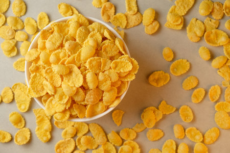 Bright yellow corn flakes scattered with a bowl overflowing with crunchy delight