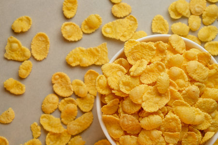 Delightful bowl of corn flakes surrounded by scattered cereal pieces