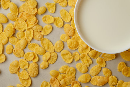Delicious and crunchy corn flakes scattered near a bowl of milkの写真素材