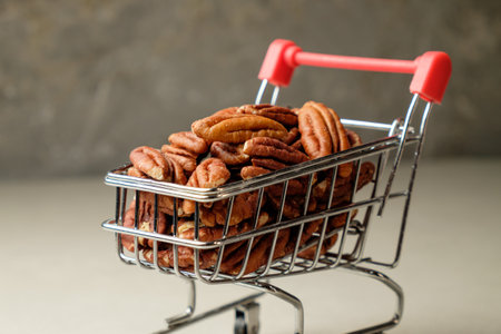 Pecan nuts overflowing from a miniature shopping cart on a neutral backgroundの写真素材