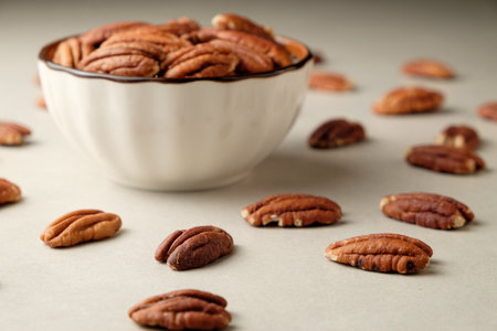 Delicious pecan nuts scattered around a charming bowl on a minimalist surfaceの写真素材