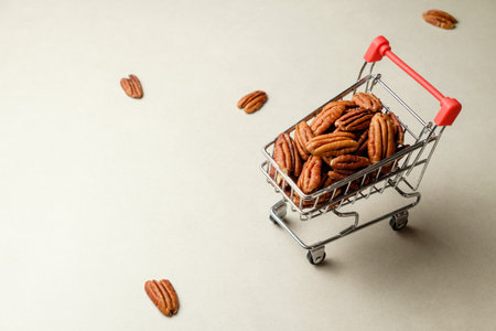 Pecan nuts in a miniature shopping cart on a soft beige backgroundの写真素材
