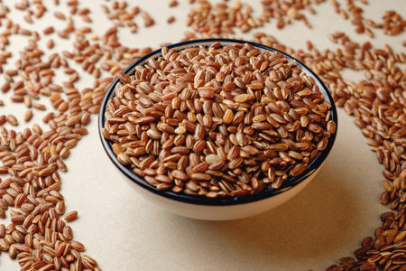 Delicious organic brown rice in a bowl surrounded by scattered grainsの写真素材