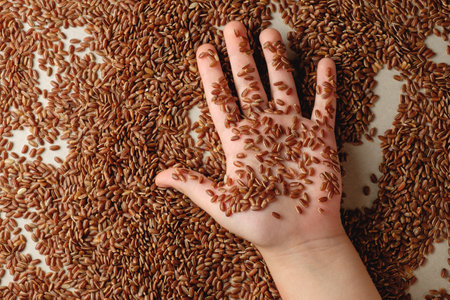Brown rice spread across a table with a hand gently grasping grainsの写真素材