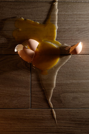 Bright yellow yolk spills across wooden floor tiles creating a striking contrast