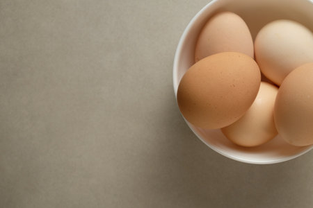 Fresh eggs in a white bowl on a neutral surface in natural light