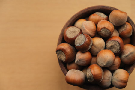 Freshly harvested hazelnuts in a rustic wooden bowl on a warm wooden tableの写真素材