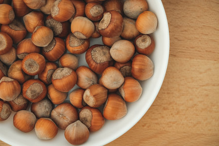 Freshly harvested hazelnuts in a white bowl on a wooden tableの写真素材
