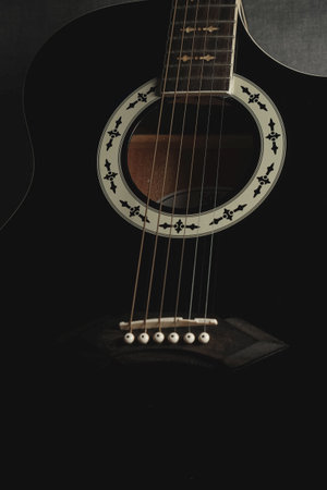 Black acoustic guitar resting on dark background showing intricate designの写真素材