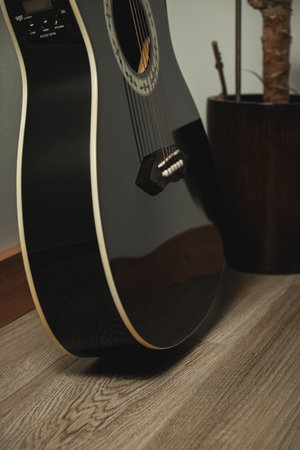 Elegant black guitar resting on wooden floor in cozy indoor settingの写真素材