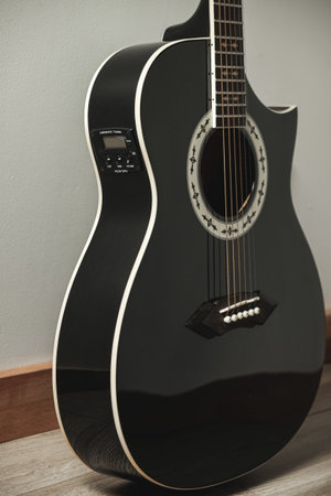 Elegant black acoustic guitar resting against a wall in soft lightingの写真素材