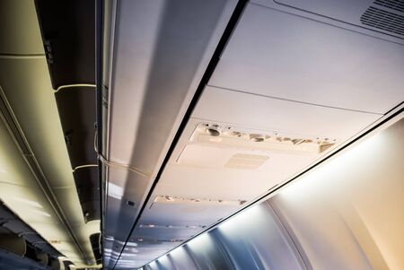 Picture of an airplane ceiling with lights, air vents, and luggage compartment doorsの写真素材