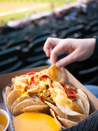 Sports Stadium Food - Person holding a tray of nachos with a female hand picking out a chipの写真素材