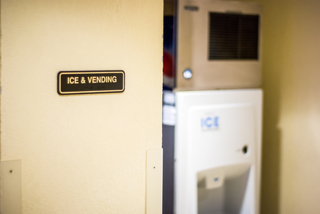 Picture of an Ice and Vending sign on a hotel wall with a slightly out of focus ice machine in the...