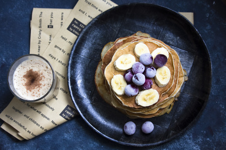 Pancakes with banana on the top and a cup of coffee flatlay