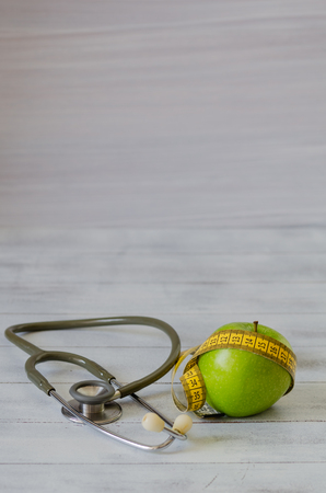 Green apple with measuring tape, stethoscope on white wooden background.Dieting concept.の写真素材